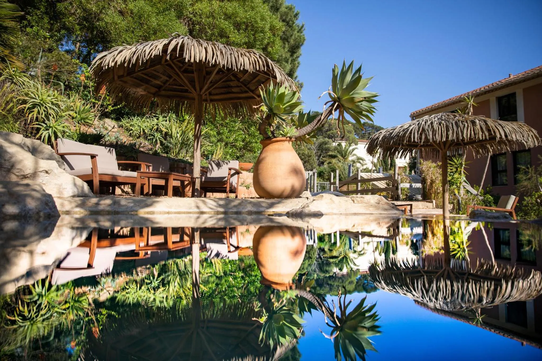 Espace de détente extérieur avec parasols en chaume et piscine.