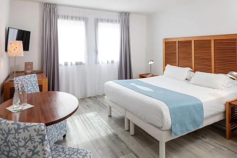 Une chambre lumineuse avec un lit double et une table.
