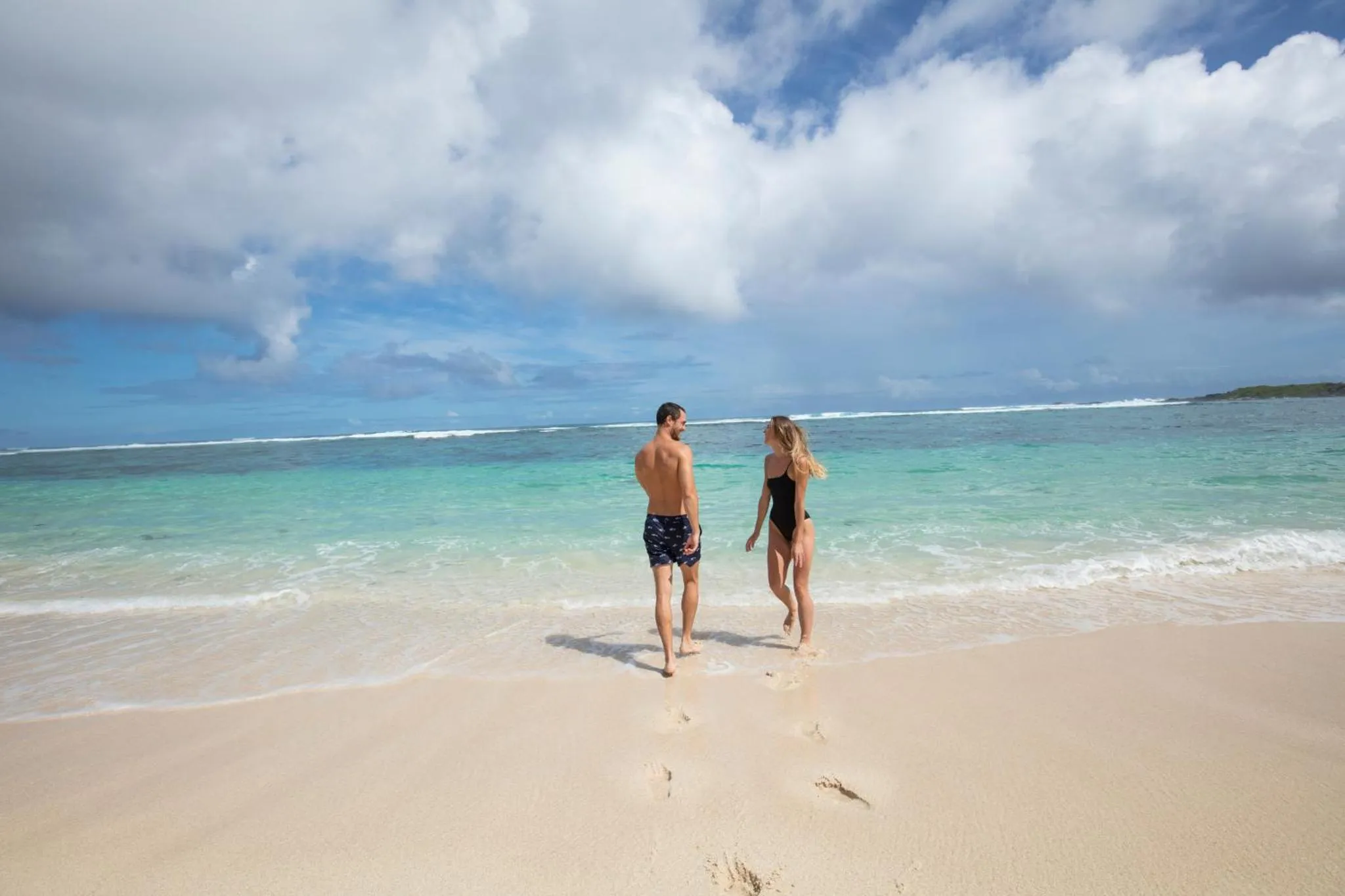 Deux personnes marchent sur une plage de sable blanc face à la mer.