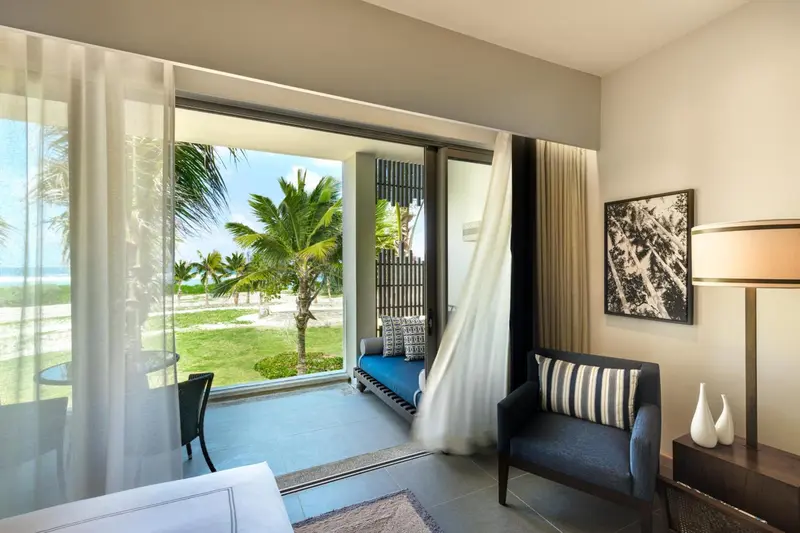 Une chambre lumineuse s'ouvre sur une terrasse avec vue sur la mer et la végétation.
