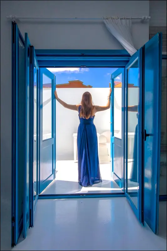 Une femme se tient sur une terrasse ensoleillée, les bras levés vers le ciel bleu.