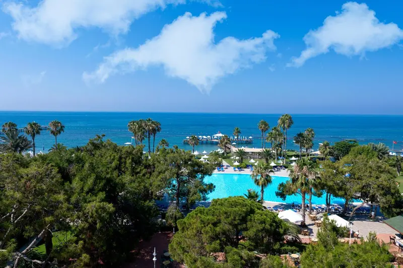 Vue aérienne d'un complexe hôtelier avec piscine et végétation luxuriante face à la mer.