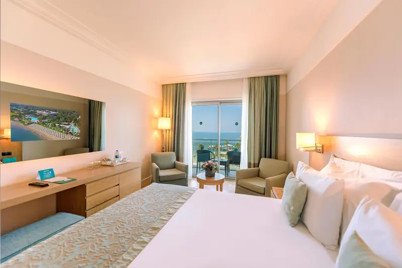 Chambre lumineuse avec un lit confortable et un accès à un balcon avec vue sur la mer.