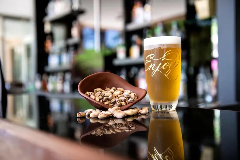 Un verre de bière blonde et un bol de pistaches sont posés sur un comptoir noir brillant.