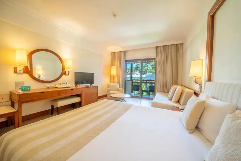 Chambre lumineuse avec un grand lit et un coin salon donnant sur une terrasse.