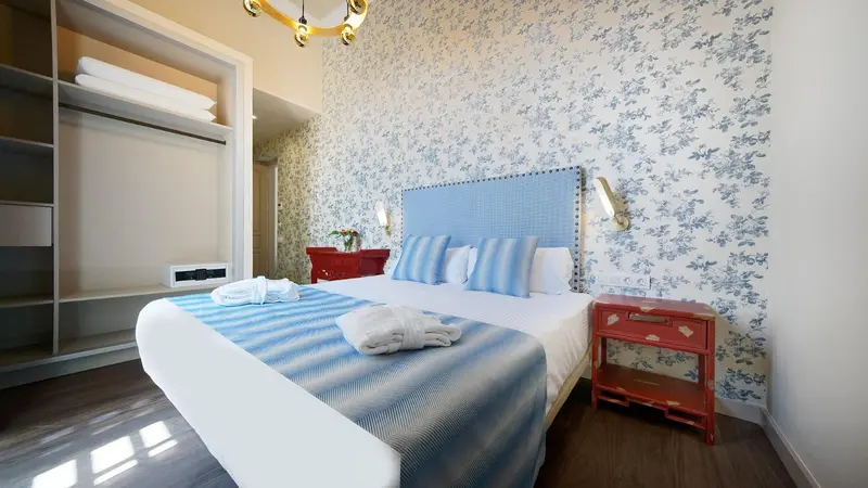 Une chambre lumineuse avec un grand lit recouvert d'une courtepointe bleue et de coussins.