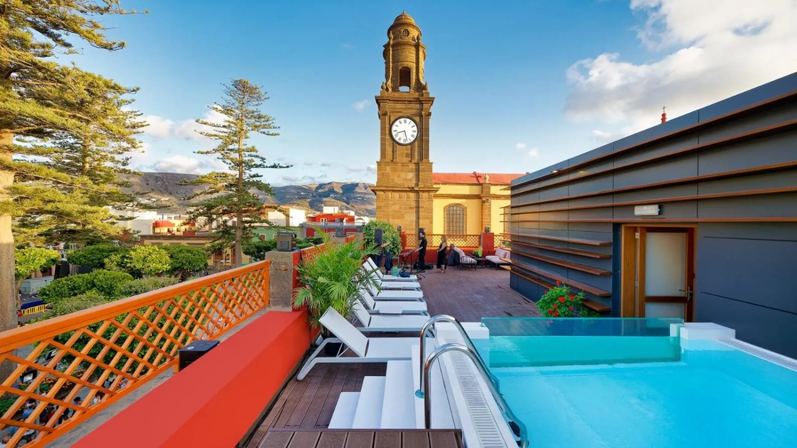 Terrasse avec transats et petite piscine face à une église et un paysage montagneux.