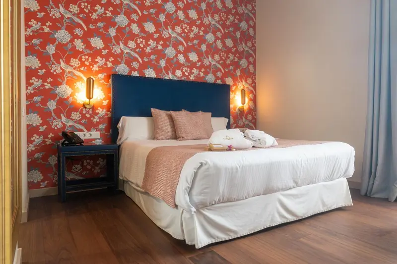 Une chambre avec un grand lit recouvert d'une couette blanche et de coussins roses.