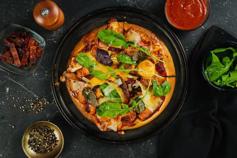 Une pizza garnie de légumes et de fromage est présentée sur une table sombre.