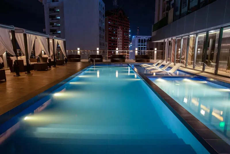 Une piscine illuminée avec des transats sur une terrasse en soirée.