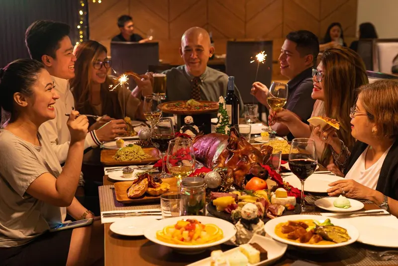 Une table festive est garnie de plats variés et de boissons, autour de laquelle sont assis des convives souriants.