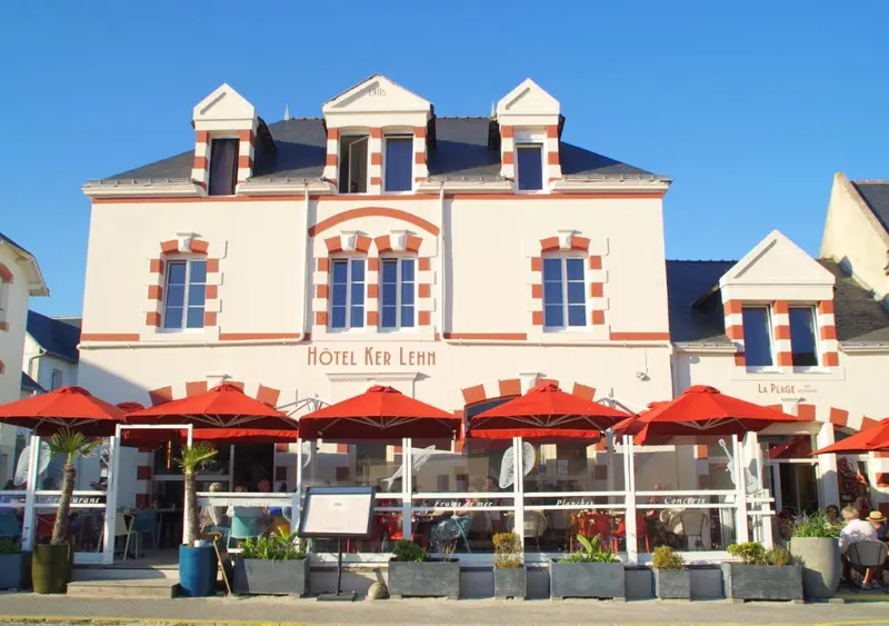 Façade d'un bâtiment blanc et rouge avec des parasols rouges devant.