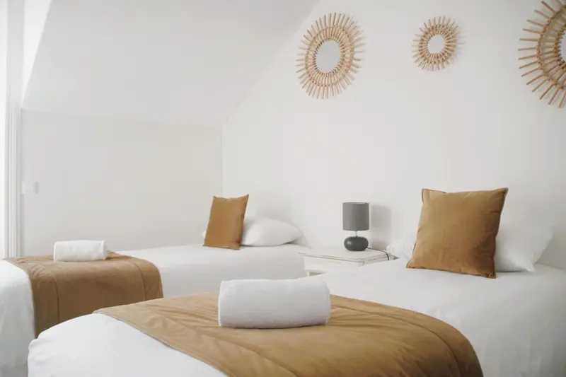 Chambre lumineuse avec deux lits simples et une décoration murale en rotin.