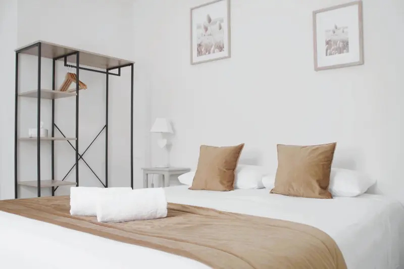 Une chambre lumineuse avec un lit fait et un portant à vêtements.
