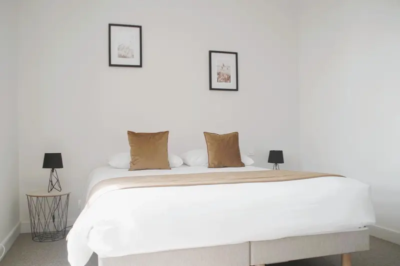 Une chambre lumineuse avec un grand lit recouvert d'une courtepointe blanche et de coussins dorés.