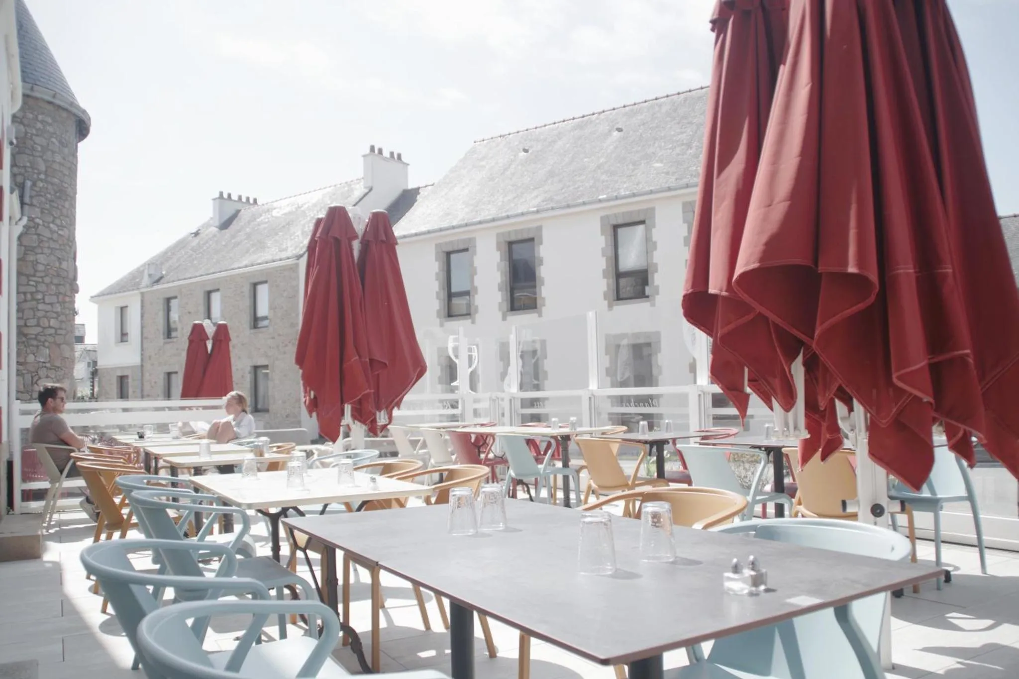 Terrasse ombragée avec tables et chaises devant un bâtiment blanc.