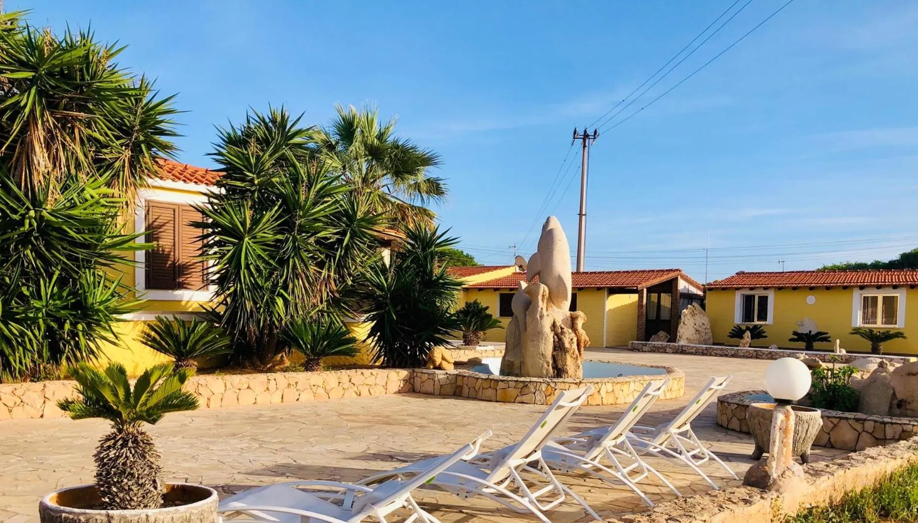 Transats blancs disposés autour d'une fontaine dans un jardin tropical.