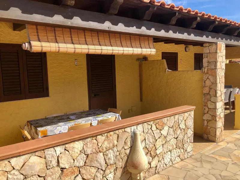 Terrasse ombragée avec table et muret en pierre.