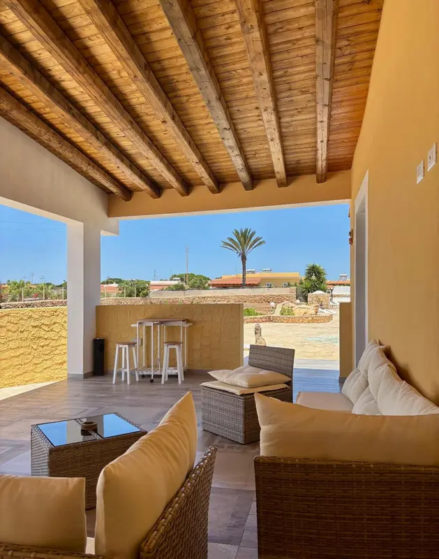 Terrasse ombragée avec mobilier de détente et vue sur un paysage côtier.