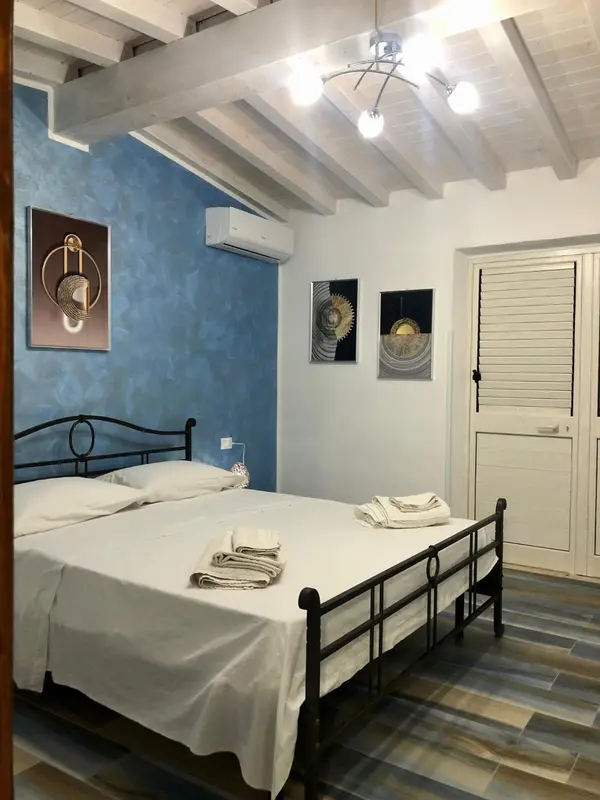Une chambre lumineuse avec un lit recouvert d'une couverture blanche et des tableaux décoratifs au mur.