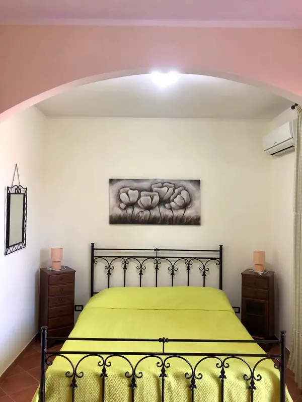 Une chambre lumineuse avec un lit recouvert d'une couverture jaune et une décoration florale au mur.