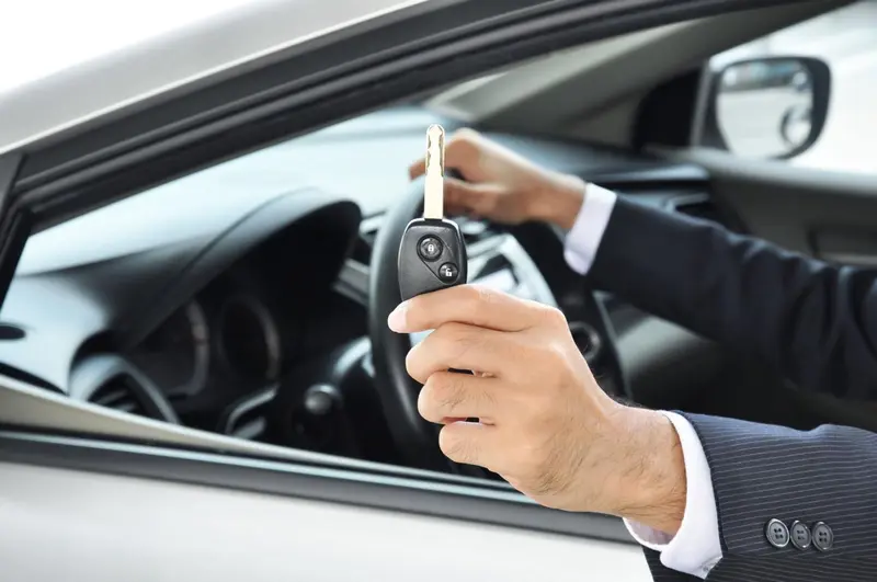 Une main tenant une clef de voiture à l'intérieur d'un véhicule.