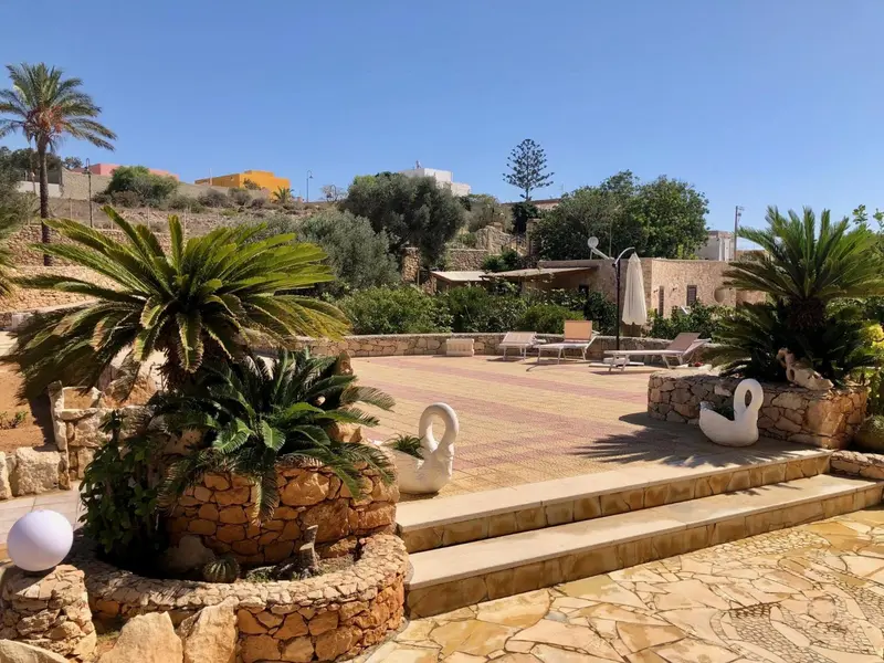 Terrasse ensoleillée avec mobilier de jardin et végétation luxuriante.