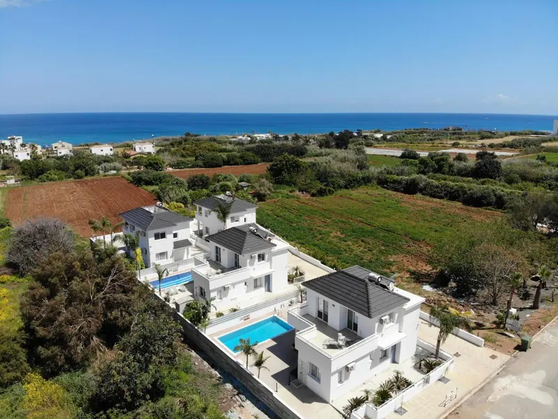 Vue aérienne de villas blanches avec piscines et végétation luxuriante face à la mer.