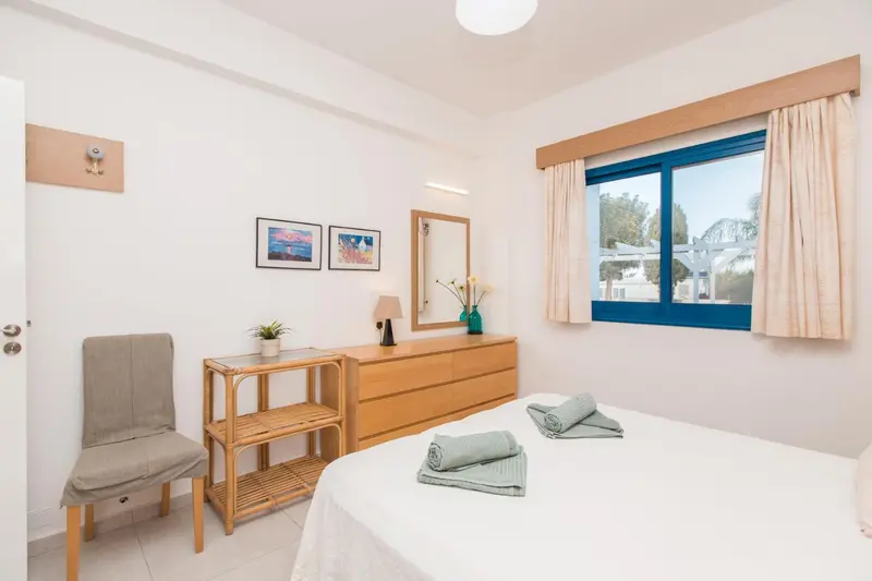 Une chambre lumineuse avec un lit fait et une commode en bois.