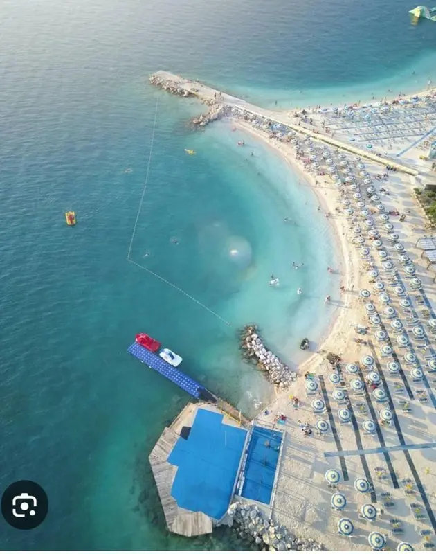 Vue aérienne d'une plage avec des transats bleus et une eau turquoise.
