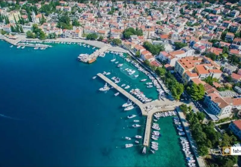 Vue aérienne d'une ville côtière avec un port de plaisance et des bâtiments aux toits rouges.