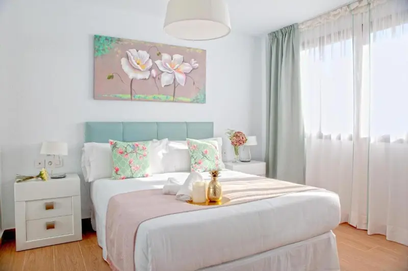Une chambre lumineuse avec un grand lit recouvert d'une courtepointe rose et de coussins fleuris.