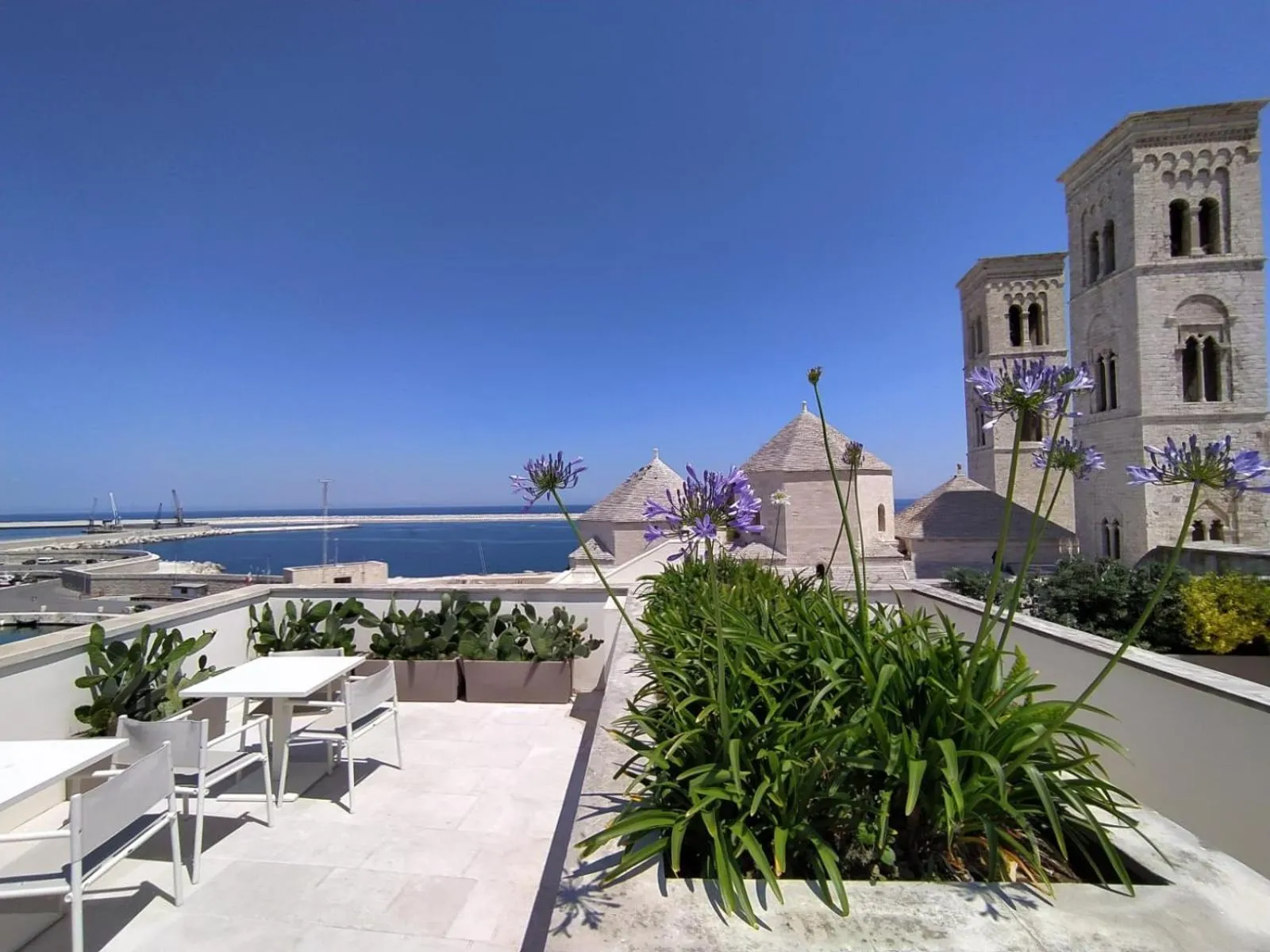 Terrasse fleurie avec vue sur la mer et des bâtiments.
