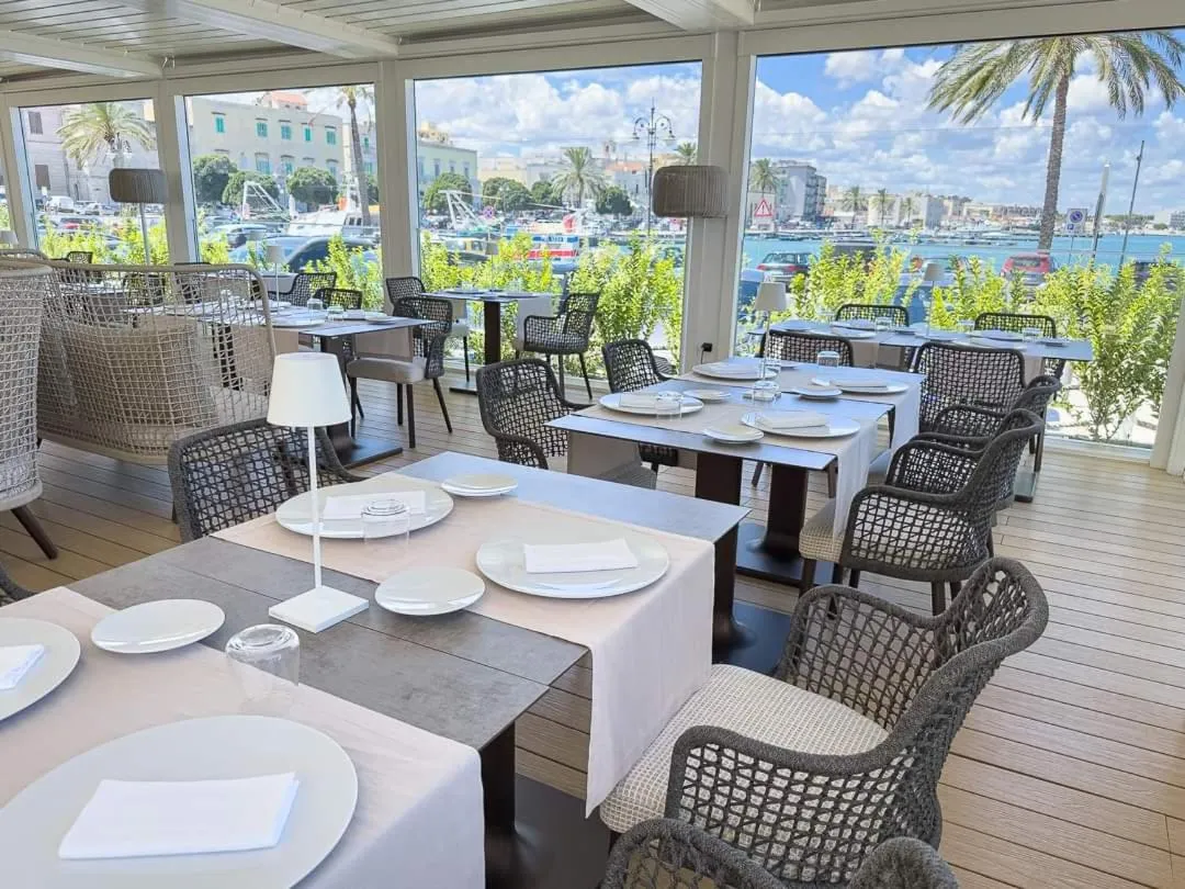 Une salle à manger lumineuse avec des tables dressées en vue sur un port de plaisance.