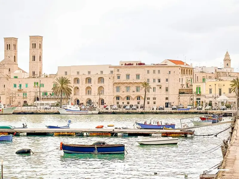 Vue d'un port de ville avec des bateaux amarrés et des bâtiments historiques en arrière-plan.