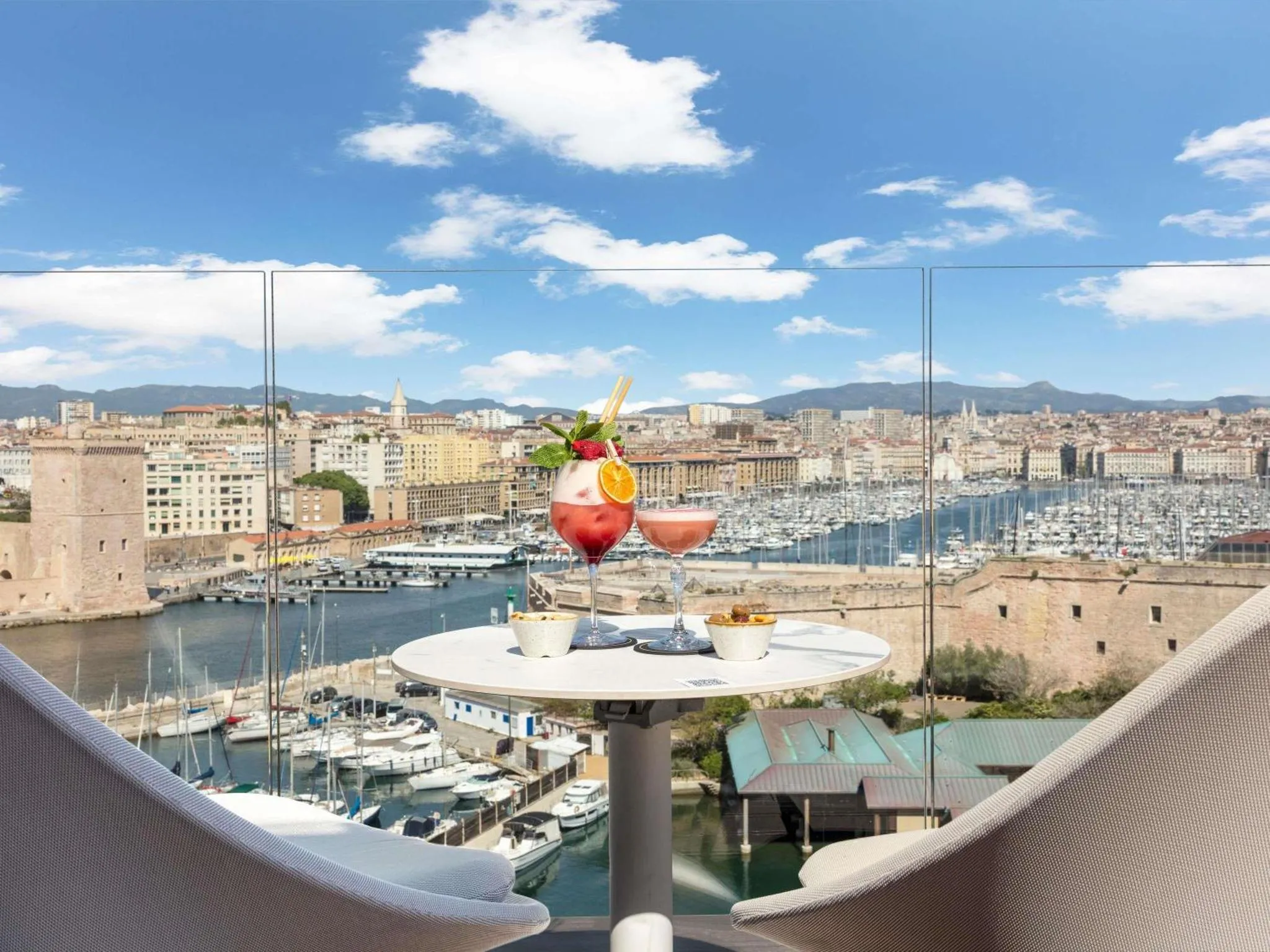 Deux cocktails colorés et des amuse-gueules sont servis sur une table ronde avec vue sur le port et la ville.