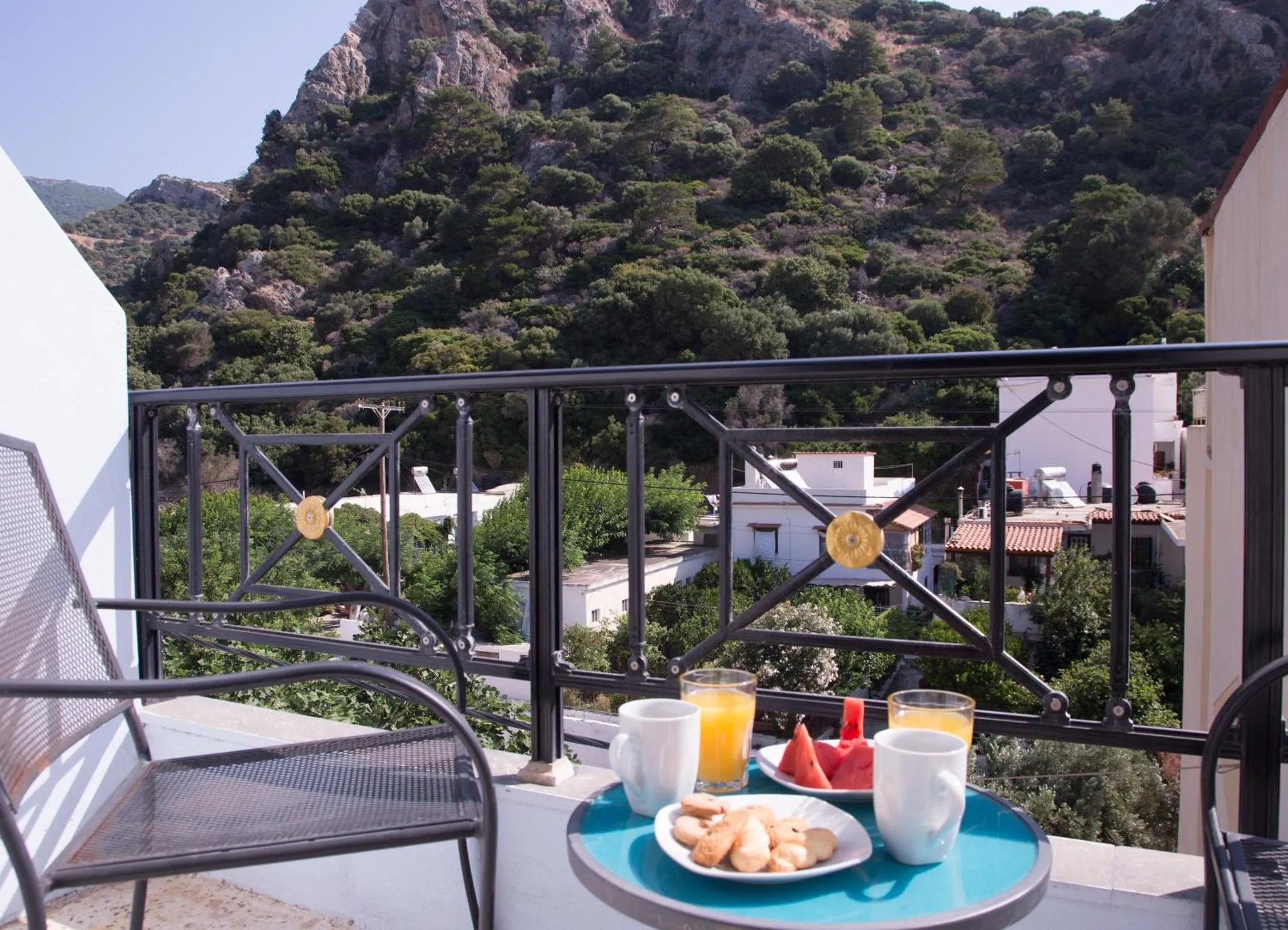 Une table basse avec des boissons et des pâtisseries est posée sur un balcon avec vue sur un paysage montagneux.