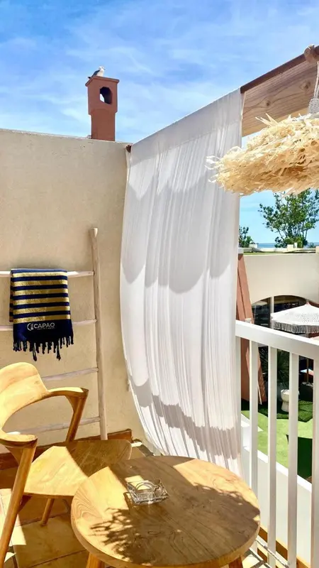 Terrasse ombragée avec mobilier en bois et rideaux vaporeux.