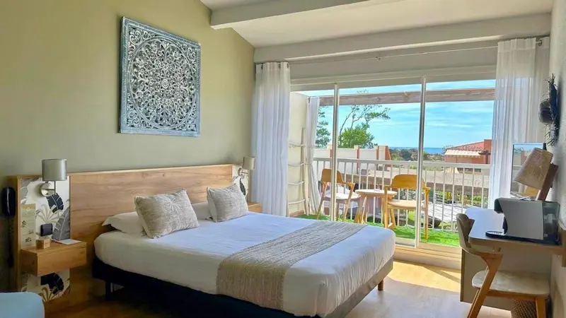 Chambre lumineuse avec un grand lit et une vue sur une terrasse ensoleillée.