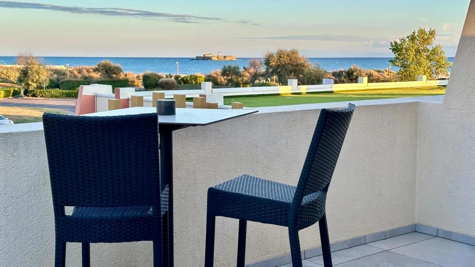 Terrasse avec table et chaises donnant sur la mer et la végétation.
