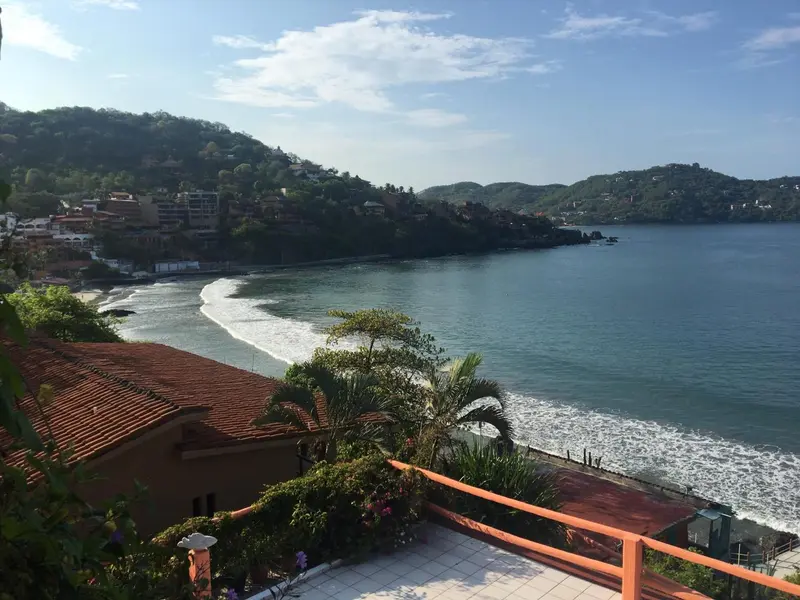 Vue d'une baie ensoleillée depuis une terrasse avec végétation luxuriante.