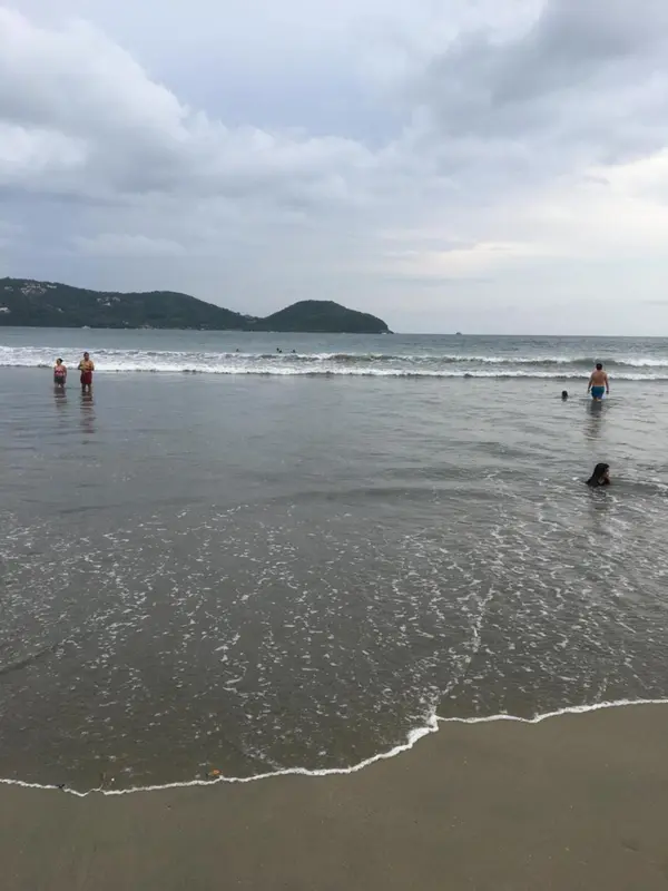 Personnes se tenant dans les vagues sur une plage de sable gris.