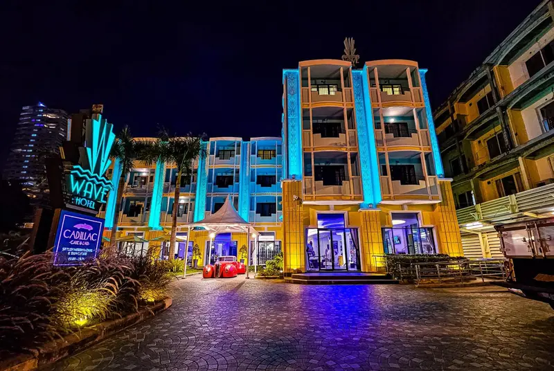 Façade d'un bâtiment illuminé de couleurs vives avec une entrée et des palmiers.
