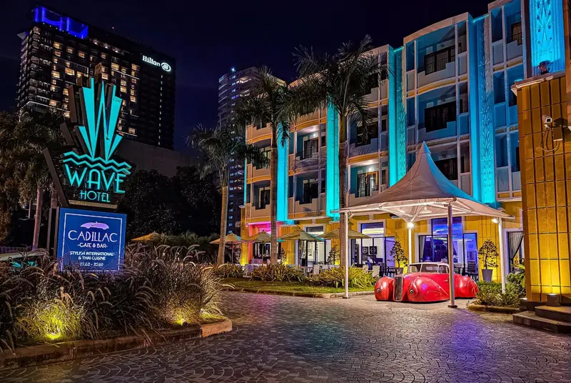 Façade d'un hôtel illuminé avec une voiture rouge vintage devant.