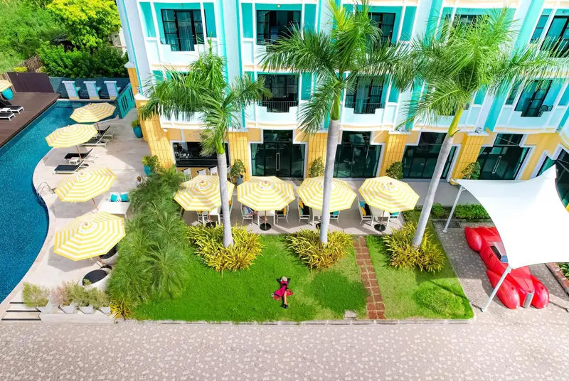 Vue aérienne d'une piscine avec transats et parasols devant un bâtiment coloré.