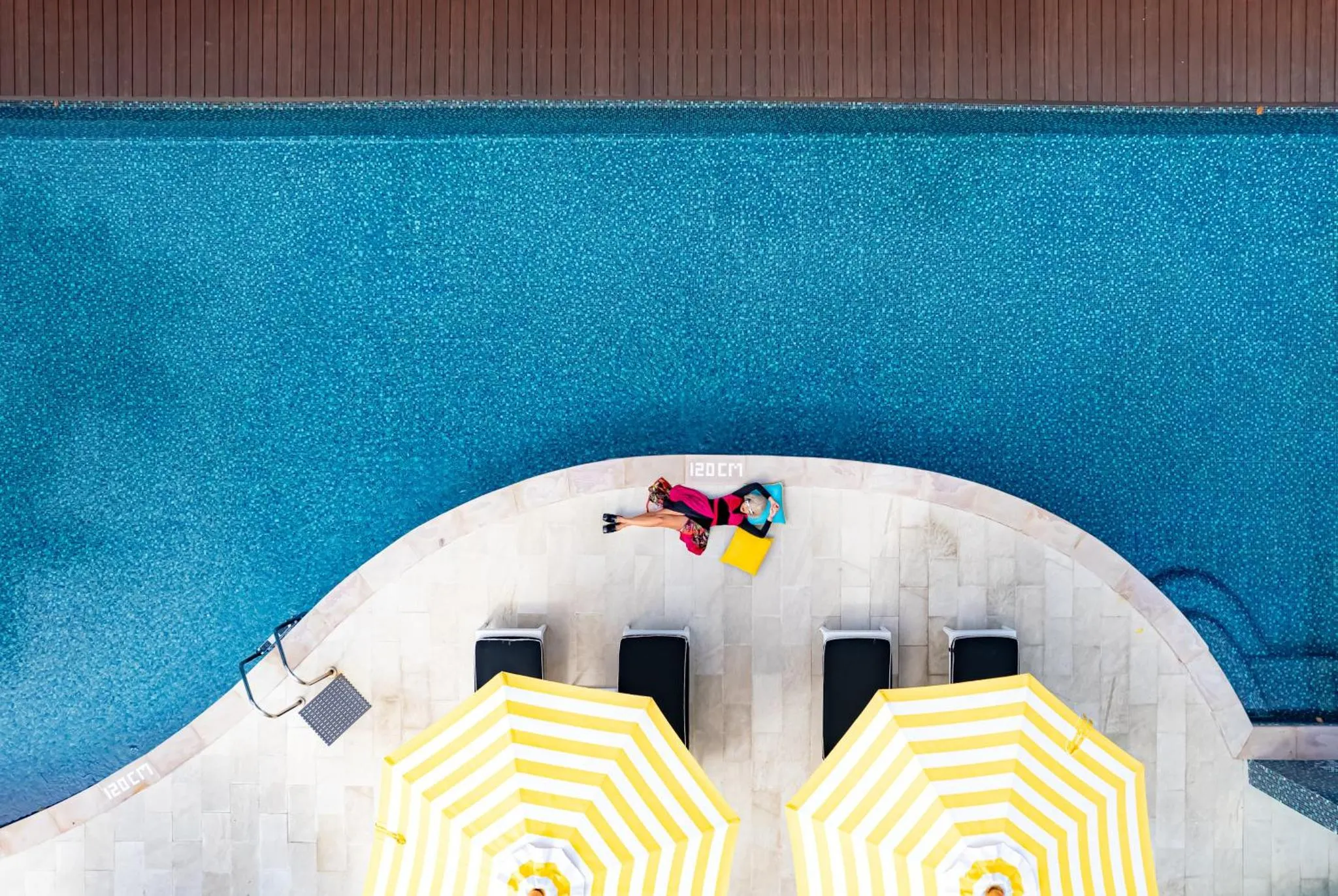 Une personne se relaxe sur un transat au bord d'une piscine rectangulaire.