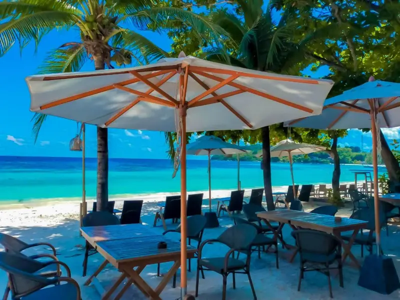 Tables et chaises sous des parasols sur une plage de sable blanc.