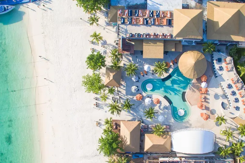 Vue aérienne d'un complexe hôtelier avec piscine et plage de sable blanc.