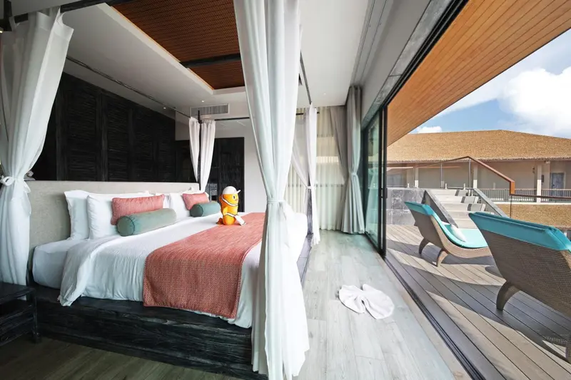 Une chambre lumineuse avec un lit recouvert de coussins et une terrasse en bois.
