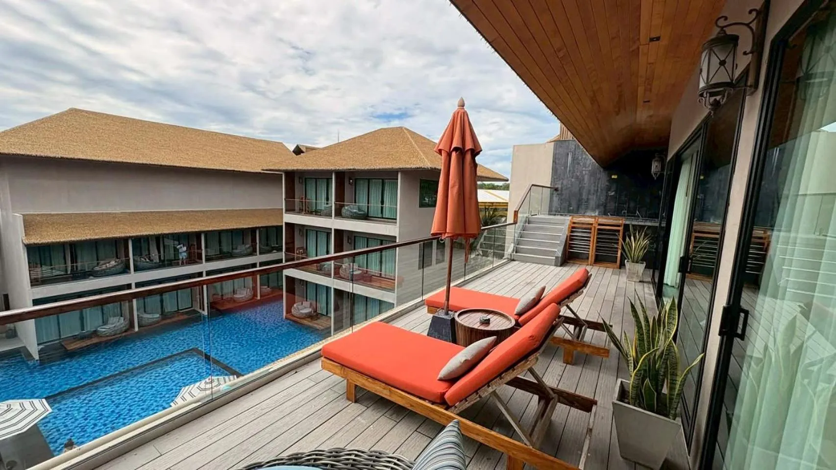 Terrasse aménagée avec transats et vue sur une piscine et des bâtiments.